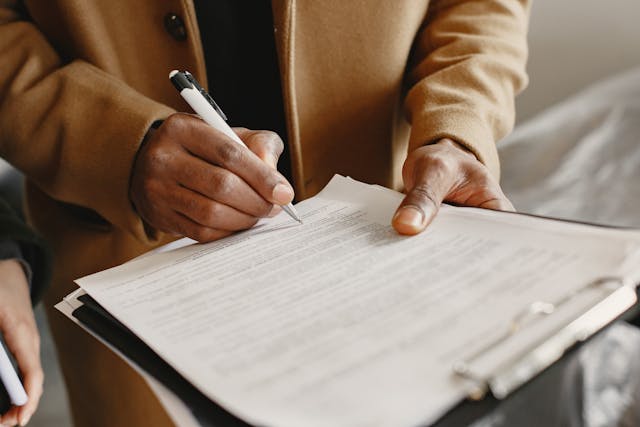 Person holding a clipboard and using a pen to write something at the bottom of the document